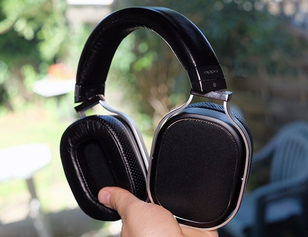 Oppo PM-1 headphones held in hand outdoors.