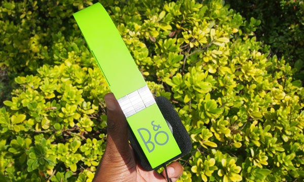 Bright green B&O Form 2i headphones held over shrubbery.
