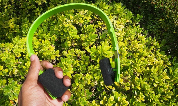 Hand holding green B&O Form 2i headphones over foliage.