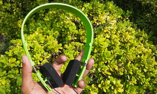 Hand holding green B&O Form 2i headphones with foliage background.
