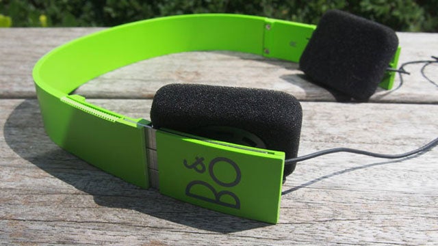 Green B&O Form 2i headphones on wooden surface.