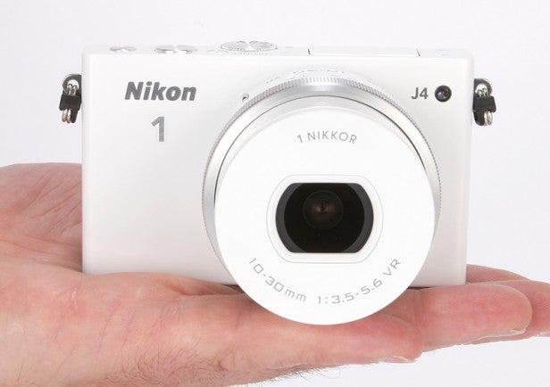 Hand holding a white Nikon 1 J4 camera.