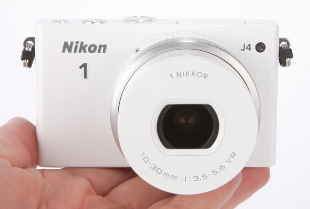 White Nikon 1 J4 camera held in a hand.