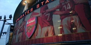 Emirates Stadium with Arsenal FC crest and player banners.