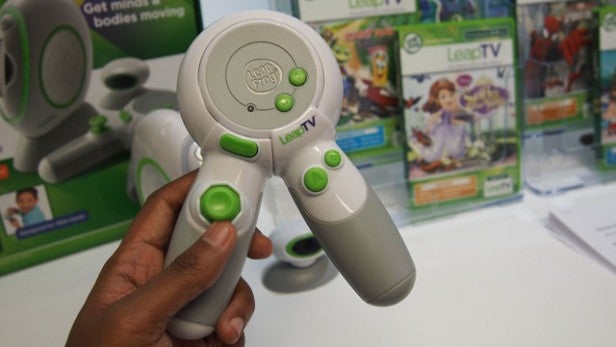 Hand holding LeapTV gaming controller with product boxes in background.