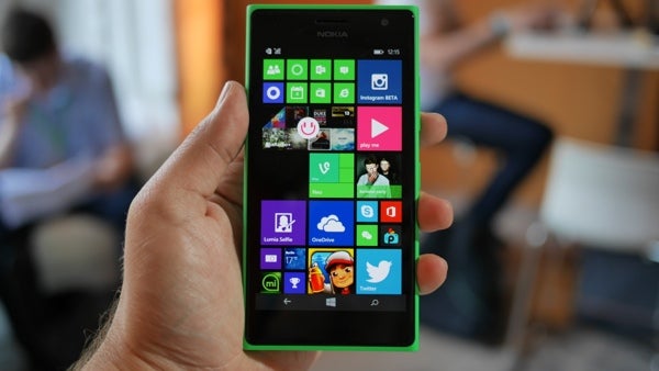 Hand holding a Nokia Lumia 735 displaying apps on screen.