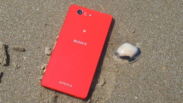 Red Sony Xperia smartphone lying on sandy beach next to a seashell.