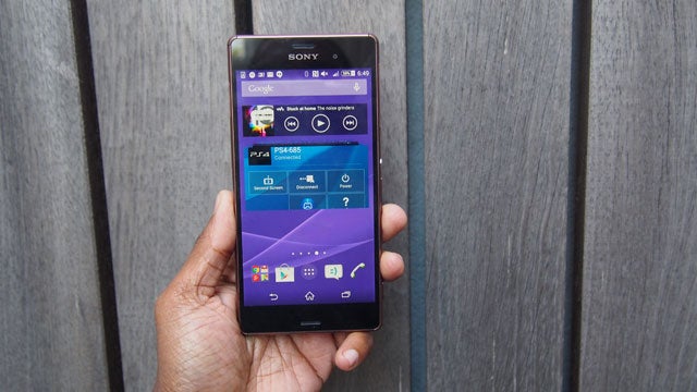 Hand holding Sony Xperia Z3 smartphone against wooden background.