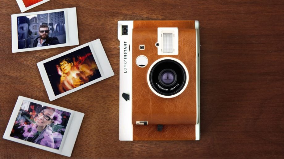 Lomo Instant camera with instant photographs on a wooden table.