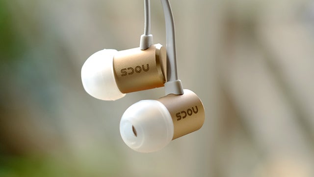 Nocs NS500 earphones suspended in air with soft focus background.