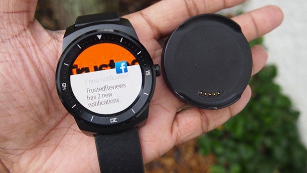 Smartwatch with notification on screen and charger in hand.