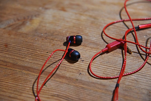 SoundMagic E10S earphones with red cable on wooden surface.
