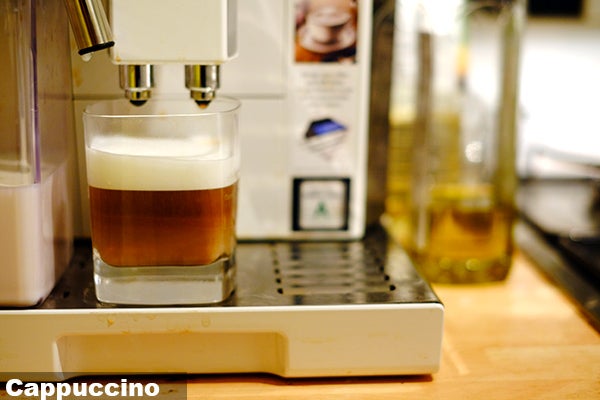 DeLonghi Eletta machine dispensing cappuccino into a glass.