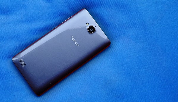 Honor 3C smartphone lying on blue fabric surface.
