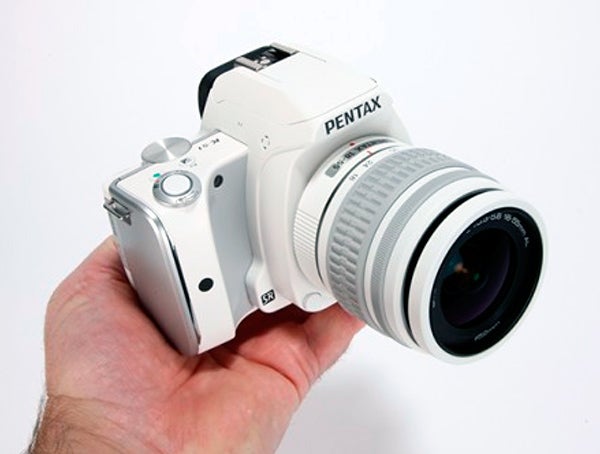 Hand holding a white Pentax K-S1 DSLR camera.