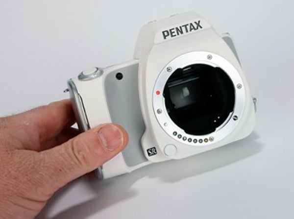 Hand holding a white Pentax K-S1 DSLR camera body.