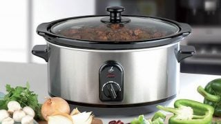 Lakeland chrome slow cooker surrounded by fresh vegetables.