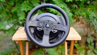 Thrustmaster T300 RS racing wheel for PlayStation on wooden stool.