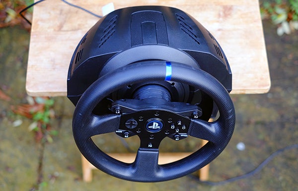 Thrustmaster T300 RS racing wheel on wooden stool outdoors.