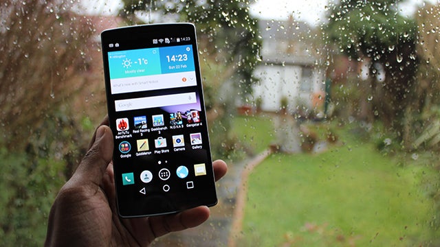 Hand holding LG G Flex 2 smartphone against rainy window.