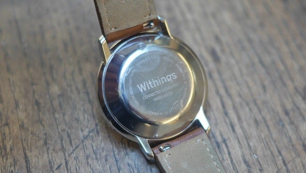 Withings Activité watch with brown leather strap on wooden surface.Withings Activité watch on a wrist with leather strap.Close-up of Withings Activité watch strap with Close-up of Withings Activité watch on wooden surface.Back of Withings Activité showing brand engraving and leather strap.