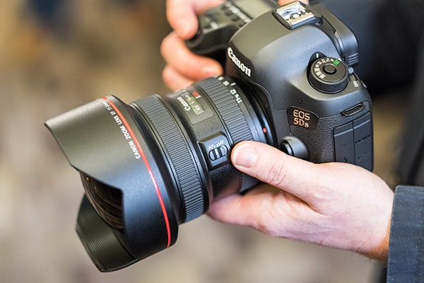 Hands holding a Canon EOS 5DS DSLR camera.Hands holding a Canon EOS 5DS camera with lens.Close-up of Canon EOS 5DS camera settings screenCanon EOS 5DS DSLR camera with red-ringed lens held in hand.Canon EOS 5DS camera with settings displayed on LCD screen