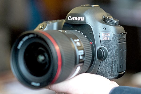 Canon EOS 5DS DSLR camera with red-ringed lens held in hand.