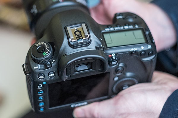 Hands holding a Canon EOS 5DS DSLR camera.Close-up of Canon EOS 5DS camera settings screenCanon EOS 5DS DSLR camera with red-ringed lens held in hand.Canon EOS 5DS camera with settings displayed on LCD screen