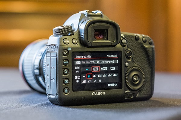 Close-up of Canon EOS 5DS camera settings screenCanon EOS 5DS DSLR camera with red-ringed lens held in hand.Canon EOS 5DS camera with settings displayed on LCD screen