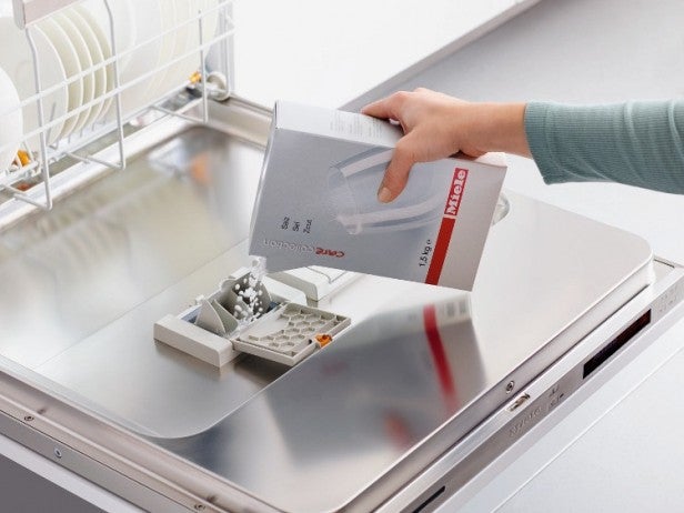 Person pouring detergent into Miele dishwasher's dispenser.
