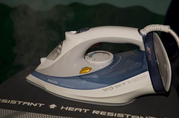 Philips Azur Performer iron emitting steam on an ironing board.