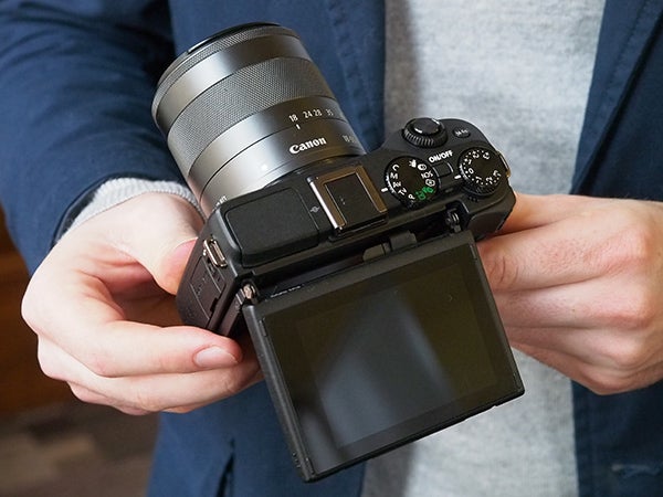 Person holding Canon EOS M3 camera with flip screen displayed.