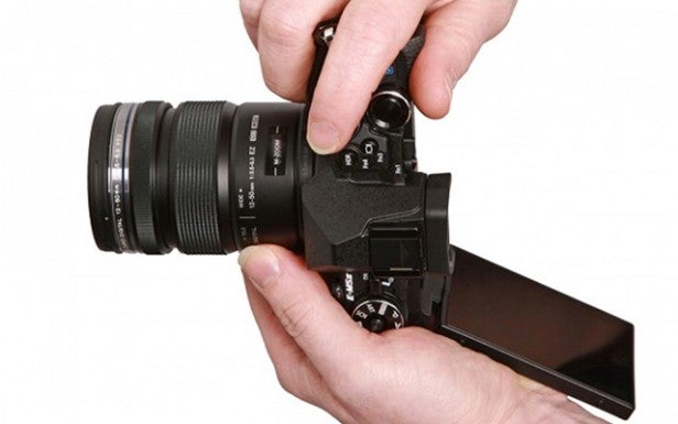 Hands adjusting lens on modern camera with articulated screen.