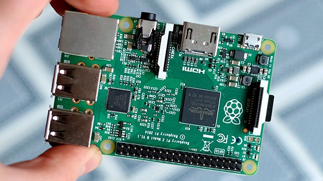 Raspberry Pi 2 circuit board held in hand over fabric.