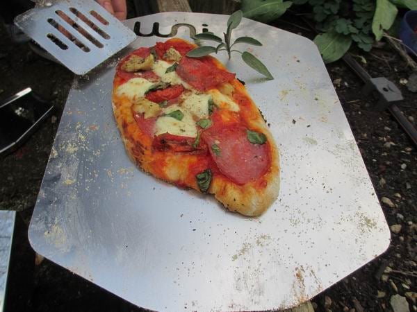Homemade pizza on a metal peel with Uuni logo.