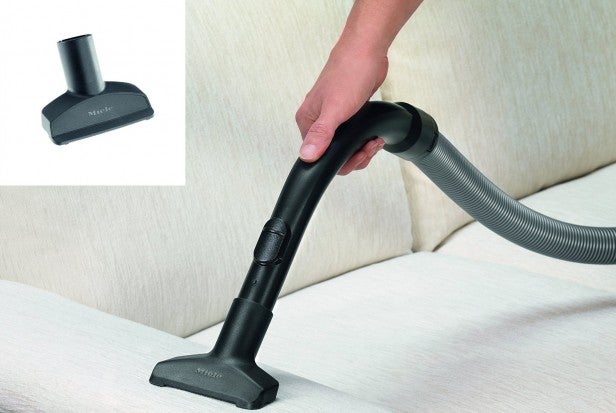 Miele vacuum cleaner being used on sofa with nozzle attachment.