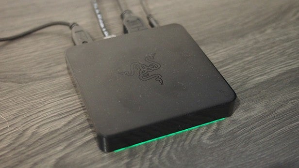 Razer Forge TV console with glowing green light on wood surface.Razer Forge TV box with glowing green light on wooden surface.