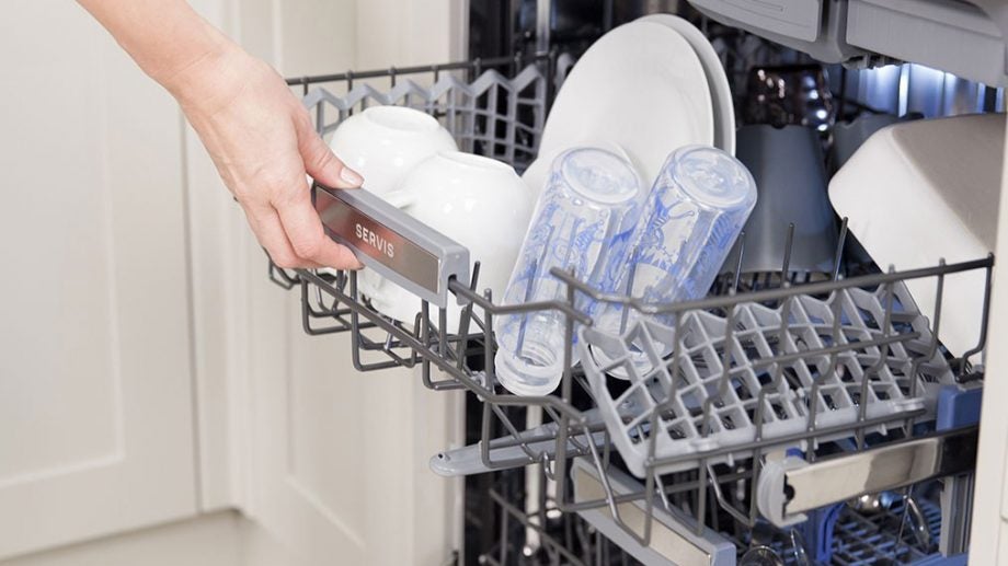 Hand opening a Servis DN61039W dishwasher full of dishes.