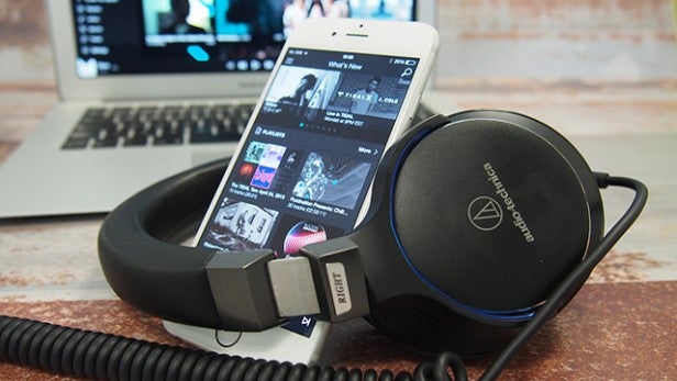 Smartphone with Tidal app beside audio headphones on desk.