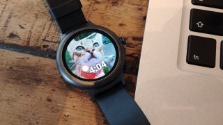 LG Watch Style displaying cat wallpaper next to a laptop.