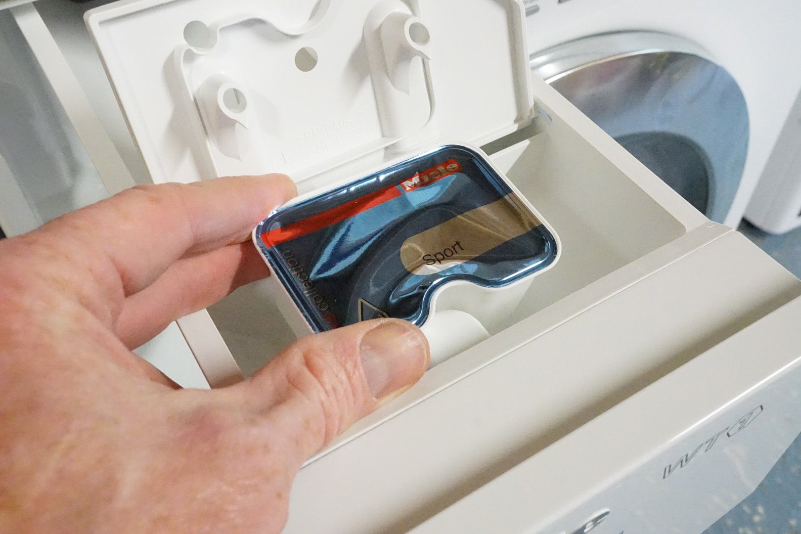 Person adding detergent to Miele WTH120 washer-dryer drawer.