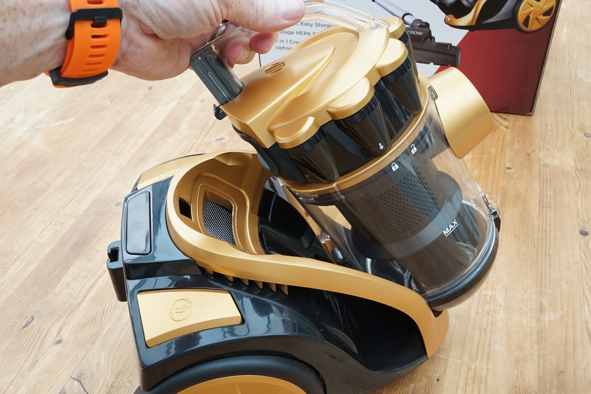 Hand removing HEPA filter from Vytronix VTBC01 vacuum cleaner on wooden floor.