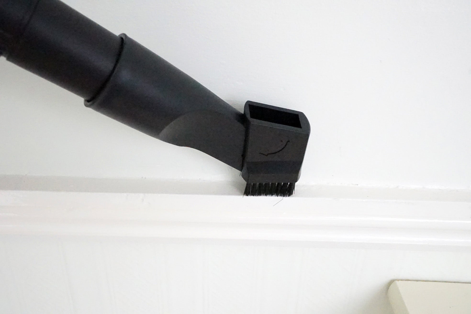 Vacuum cleaner nozzle cleaning a white baseboard.