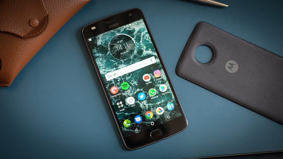 Moto Z2 Play smartphone with accessories on desk.
