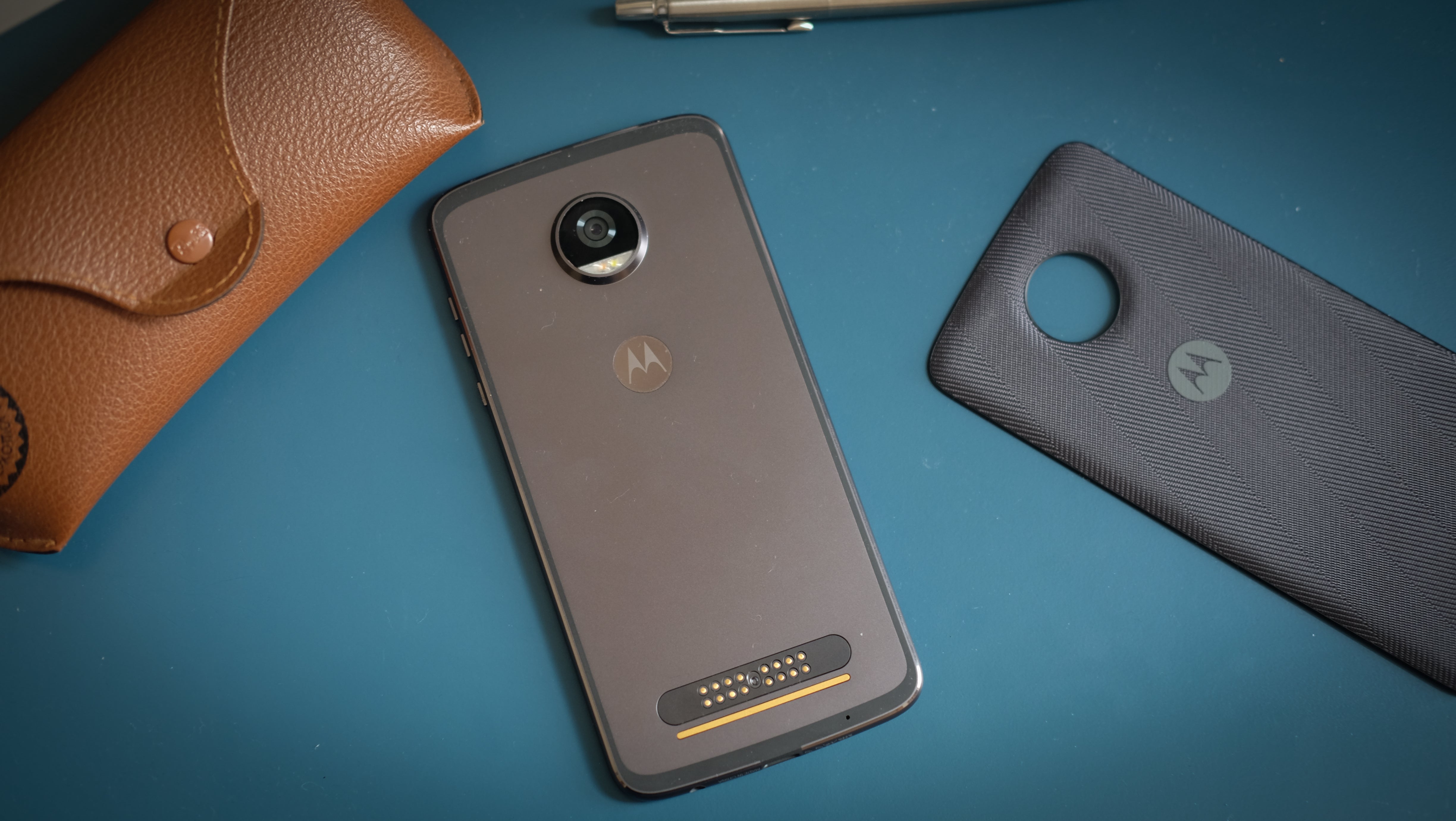 Moto Z2 Play smartphone with accessories on a blue surface.