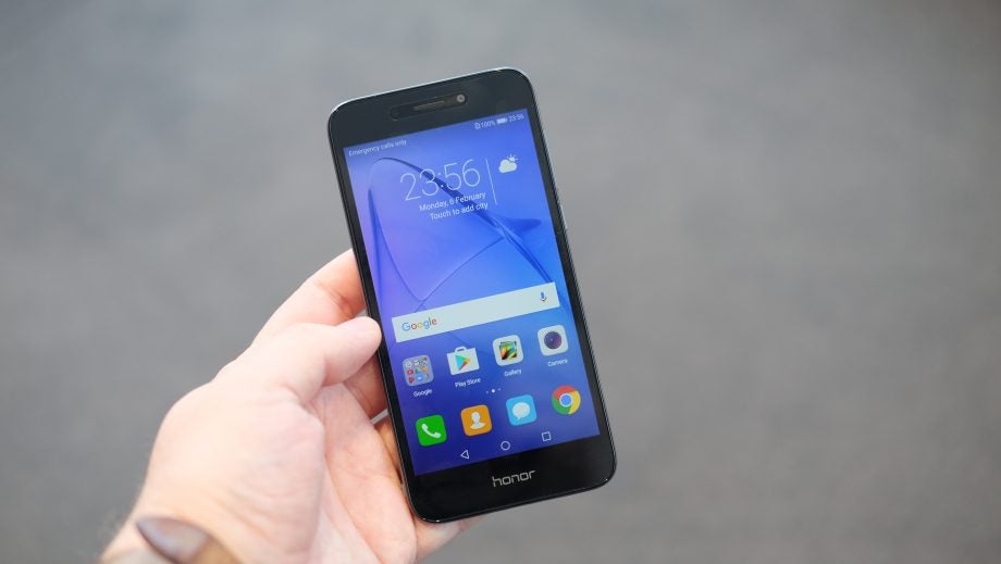 Hand holding Honor 6A smartphone displaying home screen.