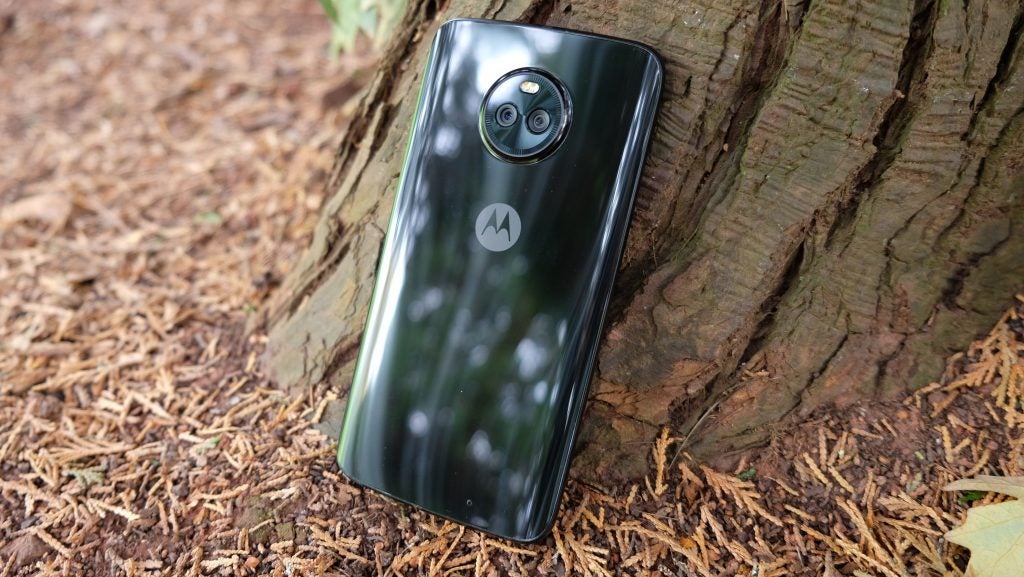 Moto X4 smartphone leaning against a tree trunk.