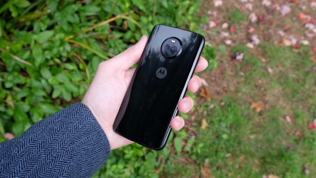 Person holding a Moto X4 smartphone outdoors.