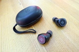 B&O Beoplay E8 earbuds and charging case on wooden surface.