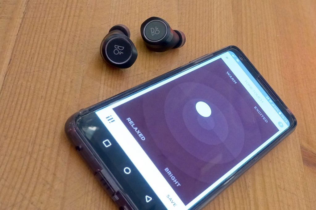 B&O Beoplay E8 earbuds next to smartphone with companion app.